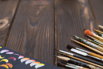 Fototapeta premium Brushes and sketches are spread out on a dark wooden surface