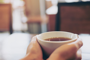 Woman holding a cup of coffee on wooden table in modern loft cafe