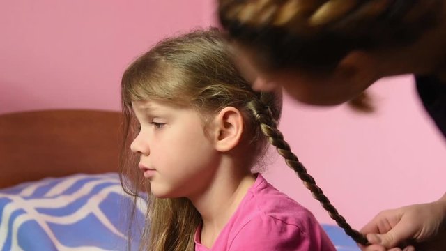 Mom braided pigtail daughter and kissed her on the cheek