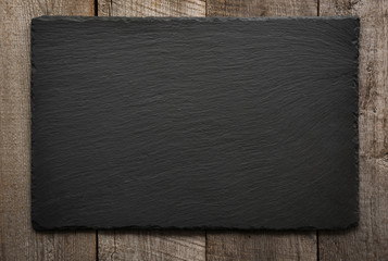 Black slate tile on wooden background. Top view. - obrazy, fototapety, plakaty