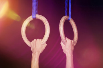 Sports, gymnastics: Two hands clutch traditional wooden gymnastic rings tightly in a gym with...