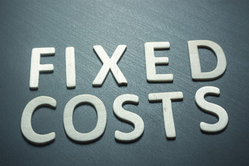 Fixed costs written with wooden letters on a green background