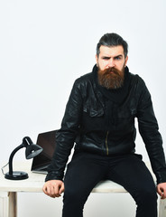 Bearded brutal caucasian hipster sitting on table with laptop on