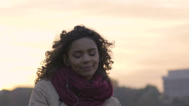 Young mixed race woman enjoying new music playlist on her smartphone at sunset