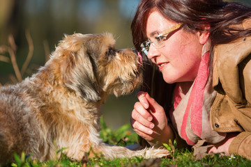 young woman lies with her dog in the grass