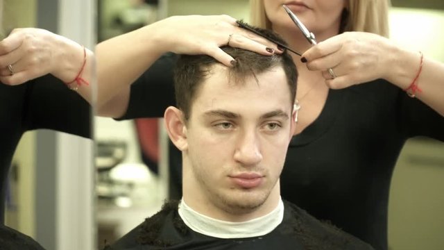 Hairdresser is making a haircut for a young man closeup