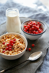 Cereals bowl decorated with currants on a wooden platter. Bottle of fresh milk in the background. Healthy breakfast.