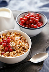 Cereals bowl decorated with currants on a wooden platter. Milk jug in the background. Healthy breakfast.