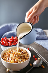 Cereals with currants on a wooden platter. Woman pouring oatmeal with milk fruit. Healthy breakfast.
