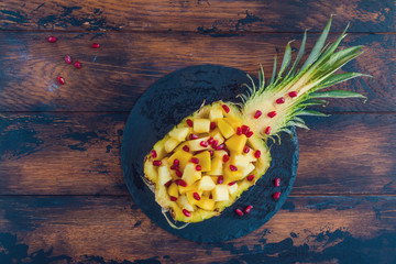 Exotic fruit salad with fresh mango, pineapple and pomegranate seeds on the rustic wooden table, top view.