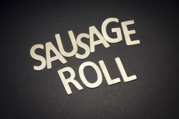 Roll of puff pastry stuffed with sausage written with wooden letters on a black background