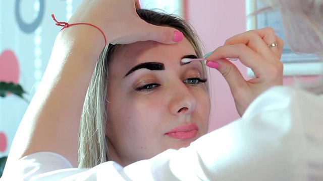 Cosmetologist washes away paint from eyebrows a Q-tip