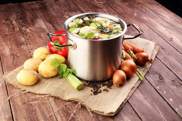 Broth with carrots, onions various fresh vegetables in a pot - colorful fresh clear spring soup. Rural kitchen scenery vegetarian bouillon or stock