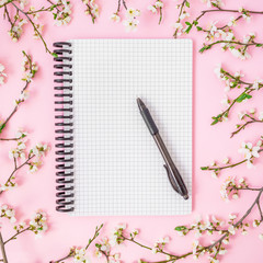 Spring flowers, notebook and pen on pink background. Flat lay, top view. Woman workspace background.