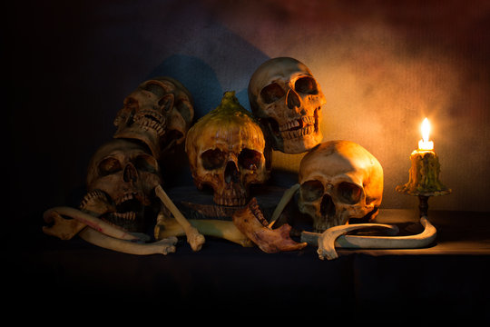 Pile of skulls and bones on wooden plate in dim light with candlelight