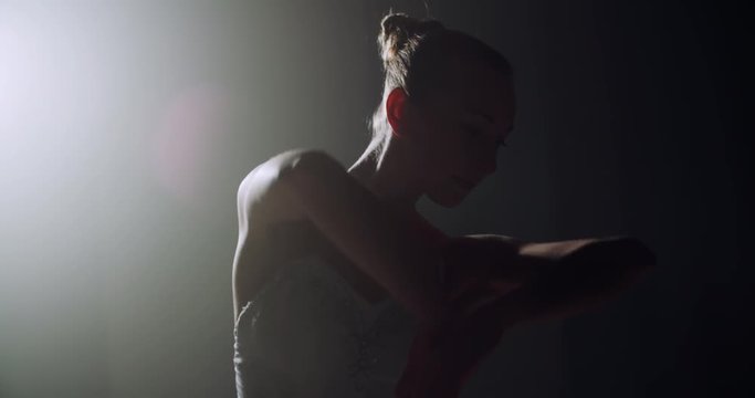 A graceful ballerina dancing ballet elements in the dark with light and smoke on the background, slow motion