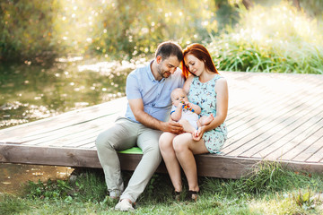 Naklejka premium Happy young family spending time together in green nature. wife with husbend and little baby. Mother and father find baby boy in basket