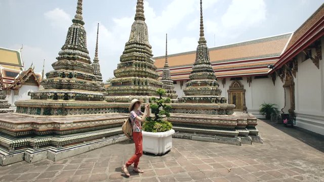 Young woman tourist taking pictures with smartphone at temple sightseeing in Bagnkok Thailand during traveling
