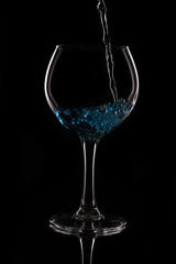 A glass with a blue liquid on a black background