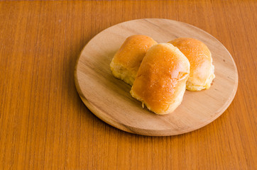 Fresh homemade baking delicious butter bun bread over wooden tray on brown teakwood floor background with sunlight on the side for happy breakfast with copy space