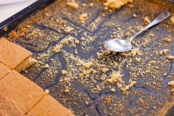Half-empty baking sheet with biscuit, crumbs and spoon