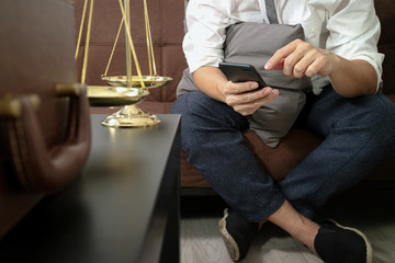 Justice and Law context.Male lawyer hand sitting on sofa and working with smart phone,digital tablet computer docking keyboard with gavel and document on living table at home