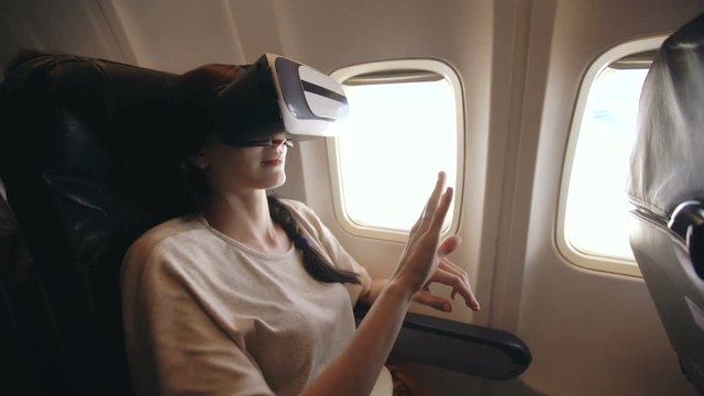 Young tourist woman relax and using VR headset for smartphone during flight in airplane
