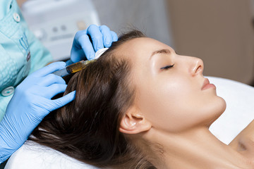 Needle mesotherapy. Cosmetic been injected in woman's head. Thrust to strengthen hair and their growth
