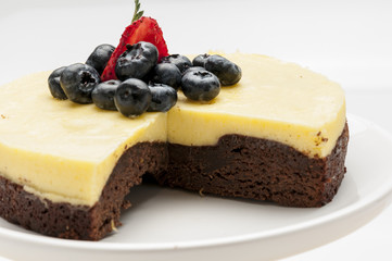 Chocolate and maracuya cake decorated with blueberries and strawberry on white plate on brown tablecloth pastry craft for social events weddings birthday catering caffe tea infusions