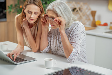 Cheerful lady teaching her mother to use laptop