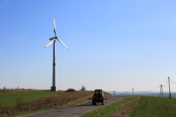 Turbina wiatrowa, wiatrak, ciągnik rolniczy na drodze.
