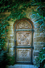 Old wooden door with carved pattern in a mysterious green garden