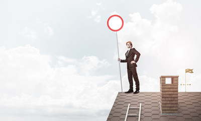 Caucasian businessman on brick house roof showing stop road sign