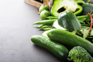 Mini cucumbers with assorted green vegetables, salad, broccoli, peas and Brussels sprouts on brown stone table top. Healthy food concept with copy space.