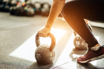 Muscular woman holding old and rusty kettle bell on to the gym floor. Focus on the kettle bell.