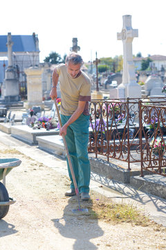 Man removing grass from path in graveyard