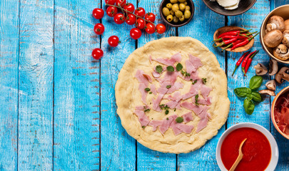 Pizza dough with ingredients on wood