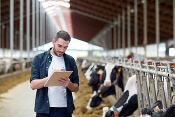 farmer with clipboard and cows in cowshed on farm