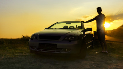 Driving into the sunset, Man silhouette standing leaned on convertible car against sunset with the countryside horizon on a summer day. concept for business, speed or success