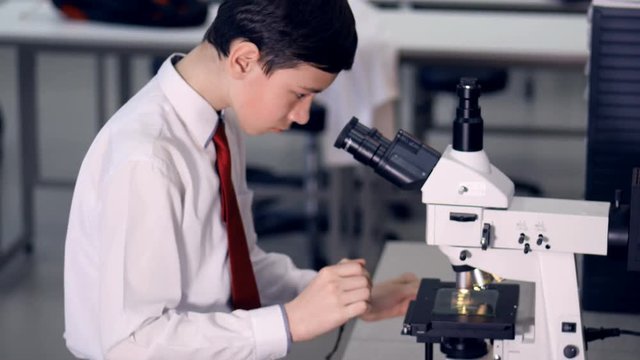 Schoolboy 10-11 years old looking at microscope in a school laboratory, making biology research. 4K.