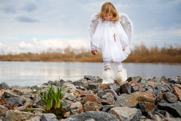 Angel boy sitting on rocks near the first spring flower