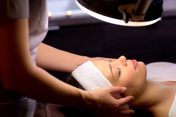 beautician doing face massage to woman at spa