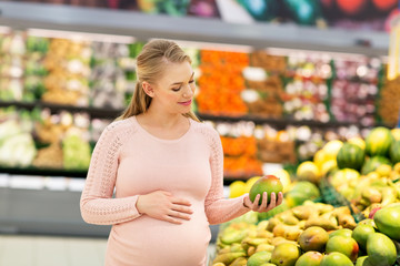 happy pregnant woman with mango at grocery store