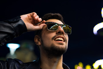 Smiling man in sunglasses with colorful reflection of night lights. Night city life