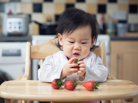 Asian baby girl eating  strawberry at home kitchen