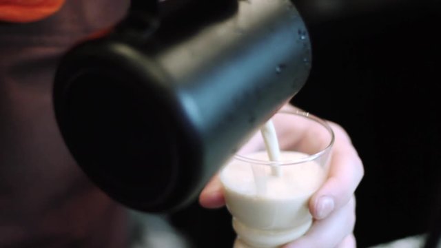 Barista pours a hot fresh coffee raf into a transparent cup a glass of black picher