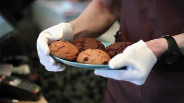 A young guy the waiter, fixes clunky cookies with chocolate crumbs and bears it to visitors to a cafe
