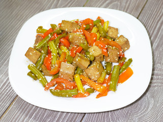 Salad with roasted tofu, paprika and green beans on white plate on  grey wooden background.