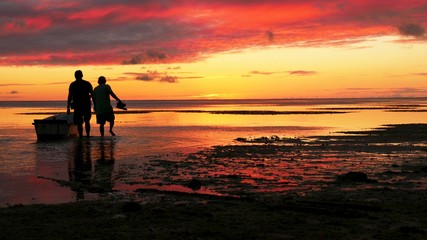 A couple of fishermen heads out to a fiery orange sunset.