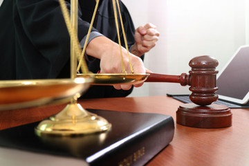 justice and law concept.Male judge in a courtroom with the gavel,working with smart phone and digital tablet computer with brass scale on wood table